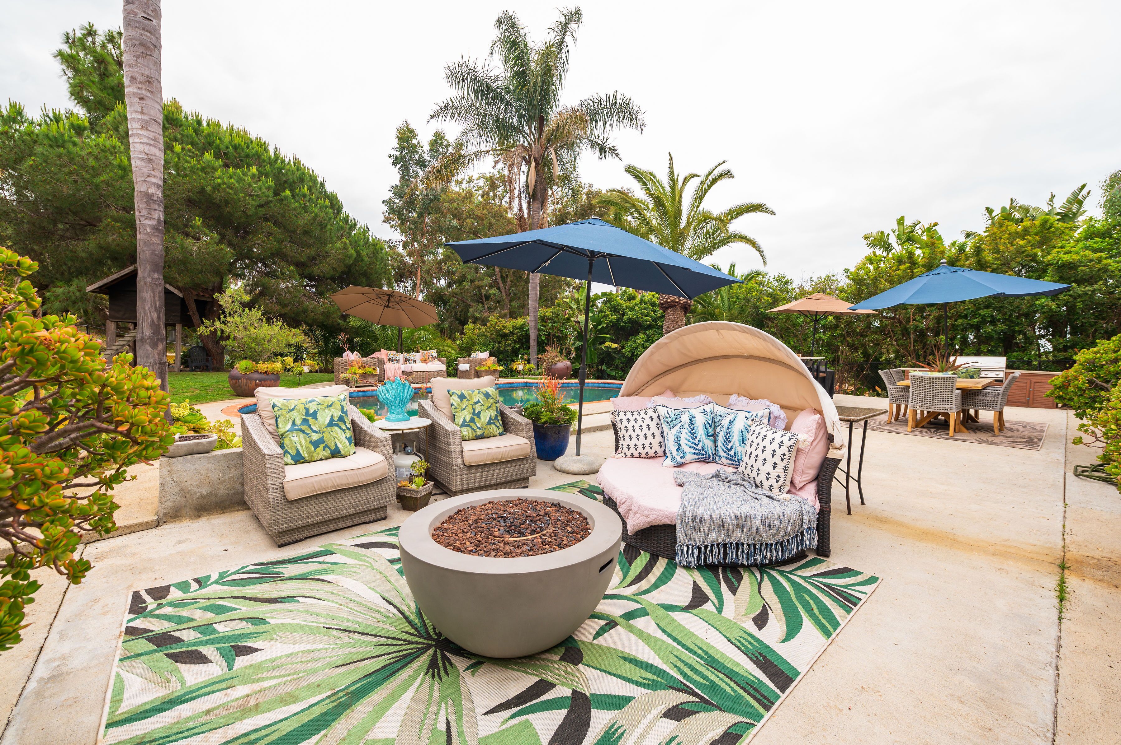Un espace extérieur aménagé en terrasse, avec des meubles en osier, un foyer et des parasols pour créer de l’ombre.