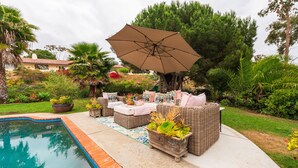 A poolside area with wicker furniture, a large umbrella, and a potted plant.