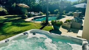 A hot tub with a pool in the background, surrounded by a well-maintained lawn and outdoor furniture.