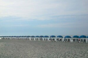 Een strand met rijen ligbedden en parasols, een hek en een heldere lucht.
