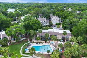 Un quartier résidentiel doté d’une piscine, entouré d’une végétation luxuriante et de nombreuses maisons.