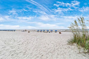 Une plage bordée de rangées de parasols bleus et de chaises longues, une plage de sable fin et un ciel dégagé.