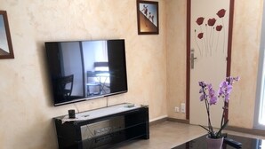 A living room with a glass-top coffee table, a flat-screen TV mounted on the wall, a black entertainment unit, and a door with a floral design.
