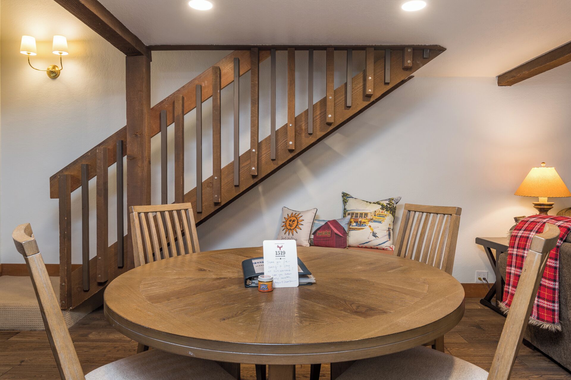 A wooden dining table with chairs, a staircase, and a lamp.