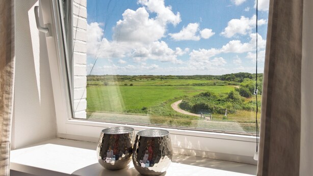 A window with two metallic vases on a sill, overlooking a green landscape with a path and trees. - Ferienwohnung in Traumhafter Lage am Naturschutzgebiet Salzwiesen (Sylt)