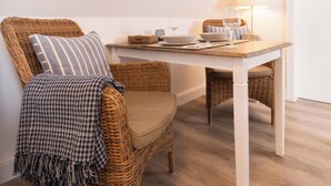 A cozy room with a dining table, wicker chairs, a lamp, and a window with a view. - Ferienwohnung in Traumhafter Lage am Naturschutzgebiet Salzwiesen (Sylt)
