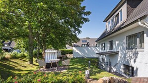 A residential area with a stone wall, a grassy lawn, and a patio with outdoor furniture. - Ferienwohnung in Traumhafter Lage am Naturschutzgebiet Salzwiesen (Sylt)