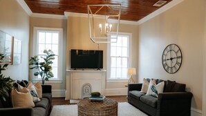 A living room with a fireplace, two sofas, a TV, and a clock on the wall.