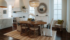 A modern kitchen with a dining area, featuring a chandelier, wicker chairs, and a marble island.