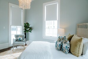 Une chambre avec un grand lit, une chaise, une plante et un lustre.