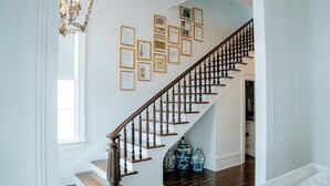 A staircase with wooden balusters, a white wall with framed documents, and a chandelier.