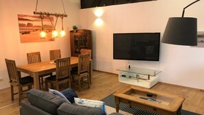 A modern living room with a dining area, a flat-screen TV, and a sofa. - Gut Strackholt - Apartment "Seemannsgarn" (Großefehn)