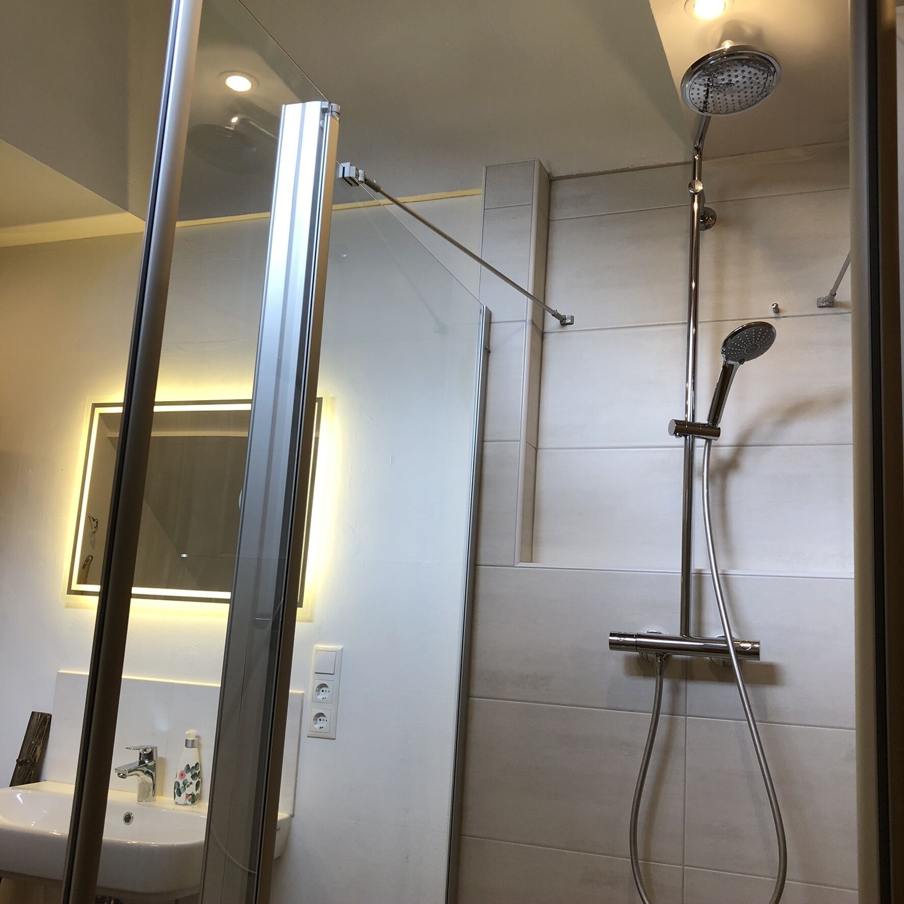 Une salle de bain moderne avec une douche à parois de verre, un lavabo avec un miroir et un luminaire fixé au mur.