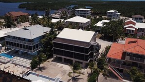Vista aérea de una zona residencial costera con varias casas de dos pisos, una piscina y palmeras.