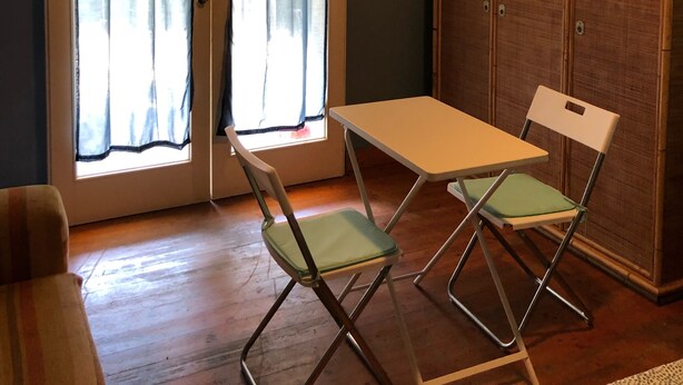 Ein Zimmer mit Holzbalkendecke, einem weißen Tisch mit zwei Stühlen, einem Kleiderschrank und einer mit Vorhängen versehenen Tür.