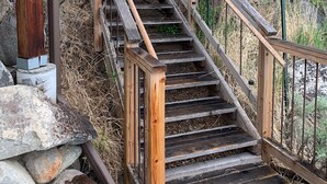 A wooden staircase with a metal railing leading up a hill, surrounded by dry vegetation and trees. - Hide-away at Yellowstone Archview (Gardiner)