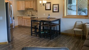 A modern kitchen with wooden cabinets, a dining table with chairs, a ceiling fan, and a window with a view of a garden. - Hide-away at Yellowstone Archview (Gardiner)
