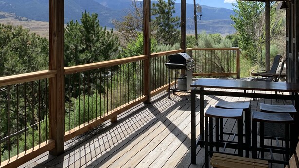A wooden deck with a view of mountains, a grill, and outdoor seating. - Hide-away at Yellowstone Archview (Gardiner)