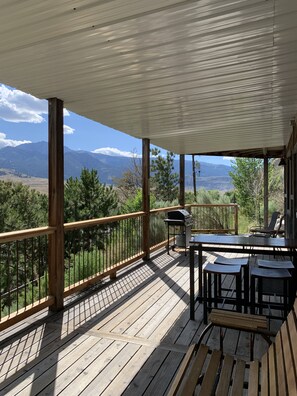 A wooden deck with a view of mountains, a grill, and outdoor seating. - Hide-away at Yellowstone Archview (Gardiner)