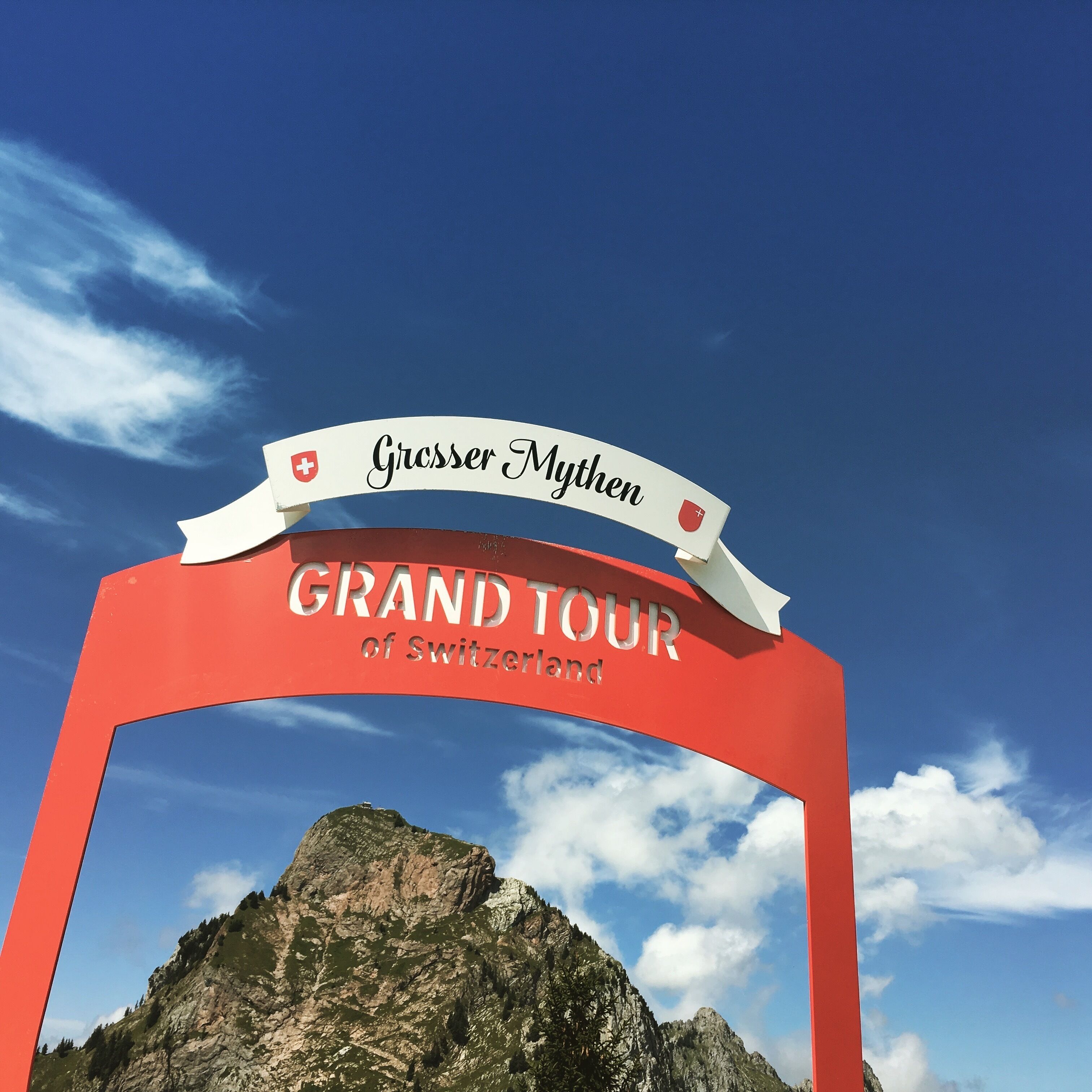 A sign for the Grand Tour of Switzerland with a mountain in the background.