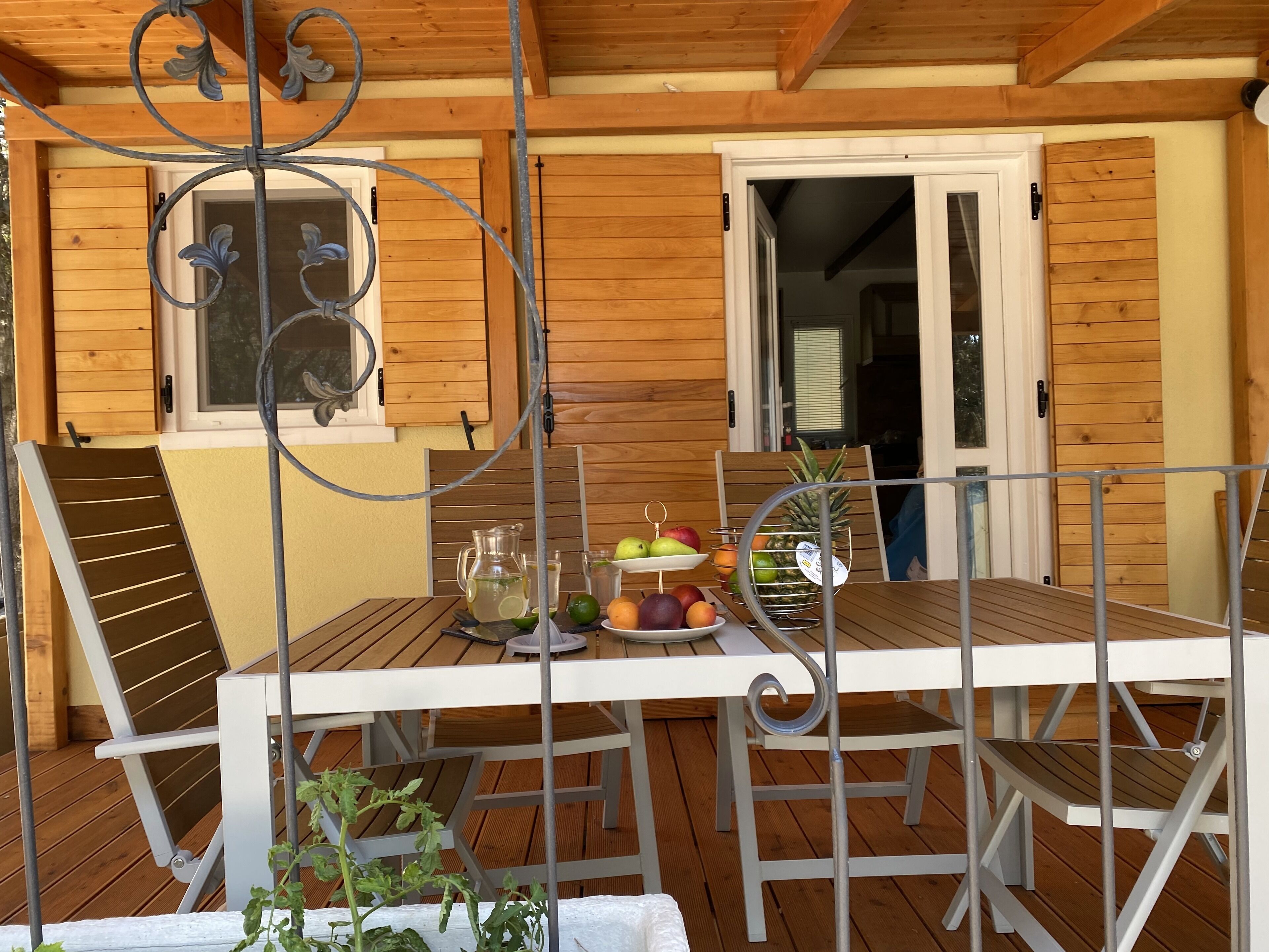 Una terraza de madera con una mesa dispuesta para comer, que incluye una jarrón, vasos y un frutero.