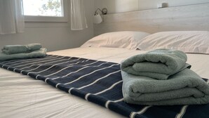 Una cama bien hecha con sábanas blancas, una manta a rayas y toallas dobladas.
