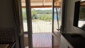 Una habitación con techo de madera, un ventanal corredero que da a una terraza exterior, un televisor sobre un mueble y un sofá estampado con motivos florales.