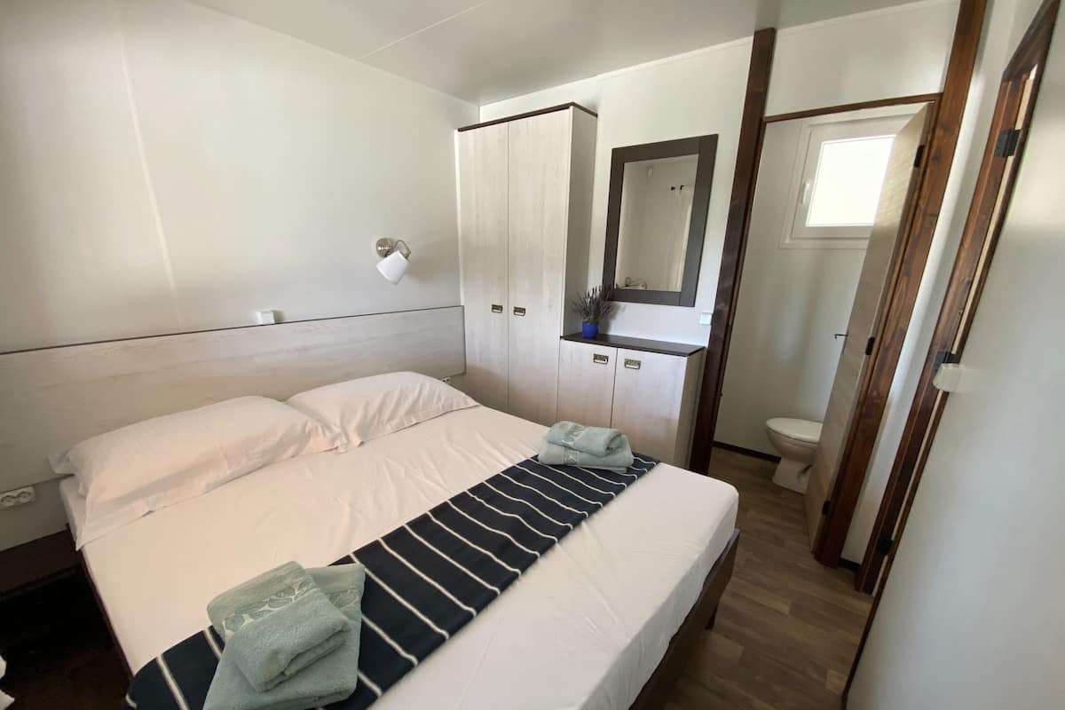 Habitación de hotel con cama, mesita de noche, espejo, armario y baño con inodoro y lavabo.