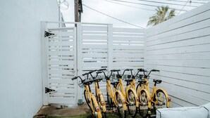 A fenced outdoor area with a row of yellow bicycles parked against a white wall. - THE PINK ROOM @emilysontheisland (Galveston)