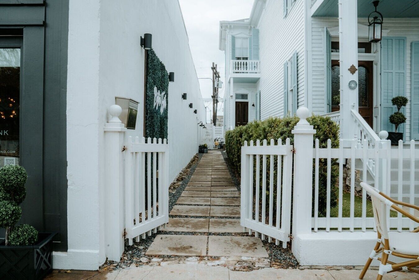 A narrow street with white fences and a staircase leading to a building with blue shutters.