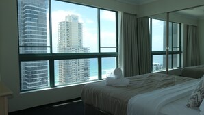 A hotel room with a large bed, a view of a cityscape, and a window with curtains. - 2 and 3 Bedroom Apartments within Crown Towers (Surfers Paradise)