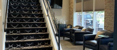 Un escalier avec des marches décorées menant à un palier, un coin salon avec des canapés en cuir et une grande fenêtre avec des stores.