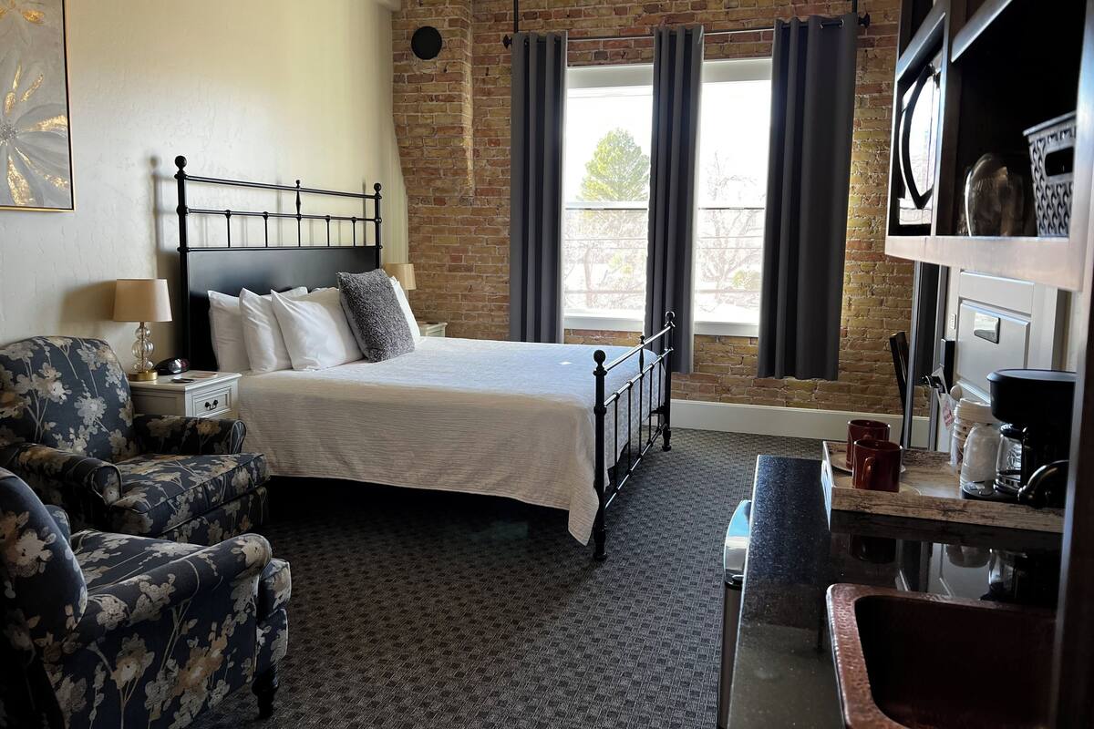 A hotel room with a bed, a chair, a desk, and a window with curtains.