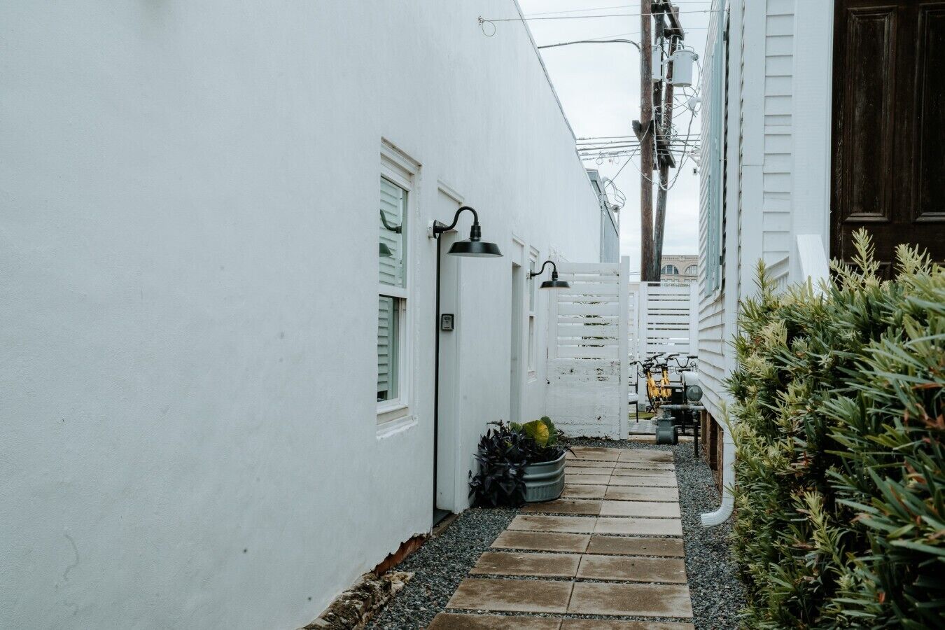 A narrow alleyway with white walls, a tiled pathway, and a small garden area with plants.