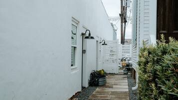 A narrow alleyway with white walls, a tiled pathway, and a small garden area with plants.