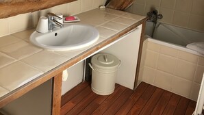 Ein kleines Badezimmer mit geneigter Decke, einem weißen Waschbecken, einer Badewanne und einer Holzbalken-Decke.