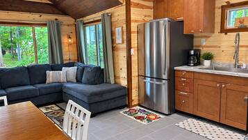 A modern log cabin interior with a sectional sofa, a stainless steel refrigerator, wooden cabinets, and a kitchen counter.