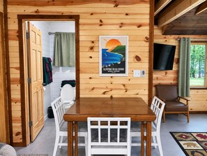 A wooden interior with a dining table, white chairs, a television, and a poster on the wall.