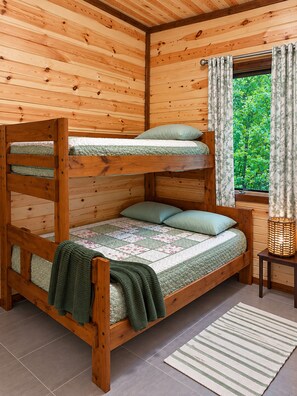 Una cama litera con colcha, almohadas y una cesta tejida sobre un piso de madera.