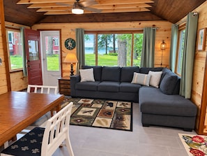 A cozy cabin interior with a sofa, dining table, and a view of the outdoors. - The Roadhouse: Lake Views▪Crystal Mountain▪Sleeping Bear Dunes▪Traverse... (Honor)