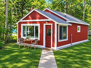 A red single-story house with a front porch, a dining area with chairs and a table, and a small window.