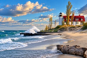 A coastal scene with a lighthouse, a red-roofed house, and a sandy beach.
