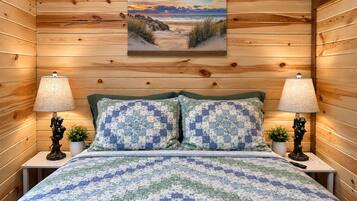 Ein Zimmer mit Holzwandverkleidung, einem Bett mit blau-weißer Steudecke, zwei Nachttischlampen und einem gerahmten Bild an der Wand.