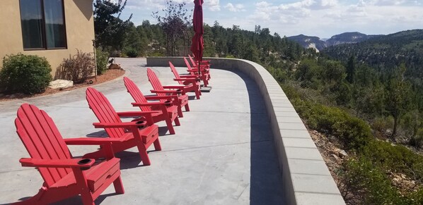 A row of red Adirondack chairs along a curved concrete path with a view of a forested mountain range. - Luxury Zion Villa, Epic Views, Gourmet kitchen, Hot tub, Great Family Retreat (Orderville)