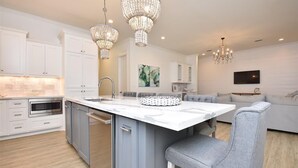 A modern kitchen with white cabinetry, a central island, and two chandeliers. - 'Saltwater Therapy' Luxurious Beach House Rental (Bolivar Peninsula)