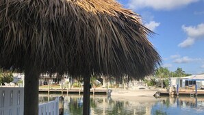 A pool area with a thatched umbrella, a wooden deck, and a view of a marina with boats. - Splash Pool- Key Colony Villa - KCB#4 (Key Colony Beach)