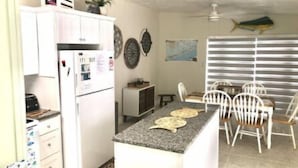 A compact kitchen with a refrigerator, a small dining table with chairs, and a fish hanging on the wall. - Splash Pool- Key Colony Villa - KCB#4 (Key Colony Beach)