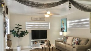 A living room with a beige sofa, a coffee table, a TV, a plant, and a ceiling fan. - Splash Pool- Key Colony Villa - KCB#4 (Key Colony Beach)