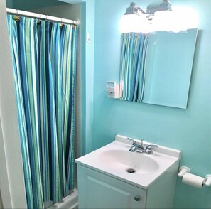 A bathroom with a white sink, a mirror, and a striped shower curtain. - Splash Pool- Key Colony Villa - KCB#4 (Key Colony Beach)