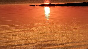 Un coucher de soleil sur une étendue d’eau calme, avec une silhouette de terre visible au loin.